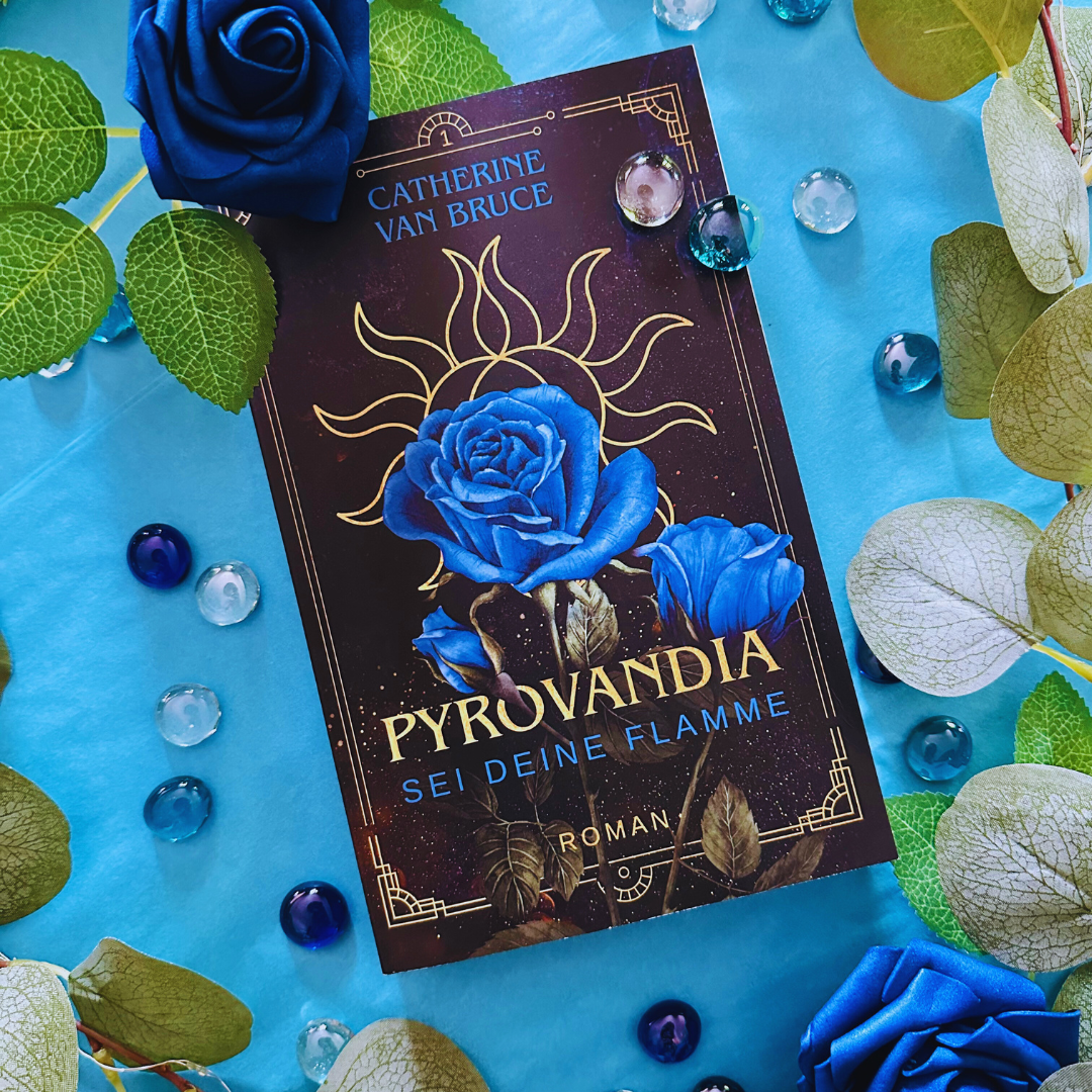 Pyrovandia Taschenbuch mit Cover mit blauer Rose und dem Symbol der beiden Sonnen darauf, sowie dem Titel Pyrovandia - Sei deine Flamme und der Nennung der Autorin Catherine van Bruce